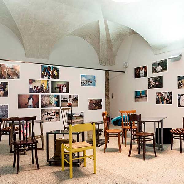 Sala interna ai Magazzini fotografici con foto a colori appese alle pareti e due tavole con sedie, utilizzabile come location per eventi.